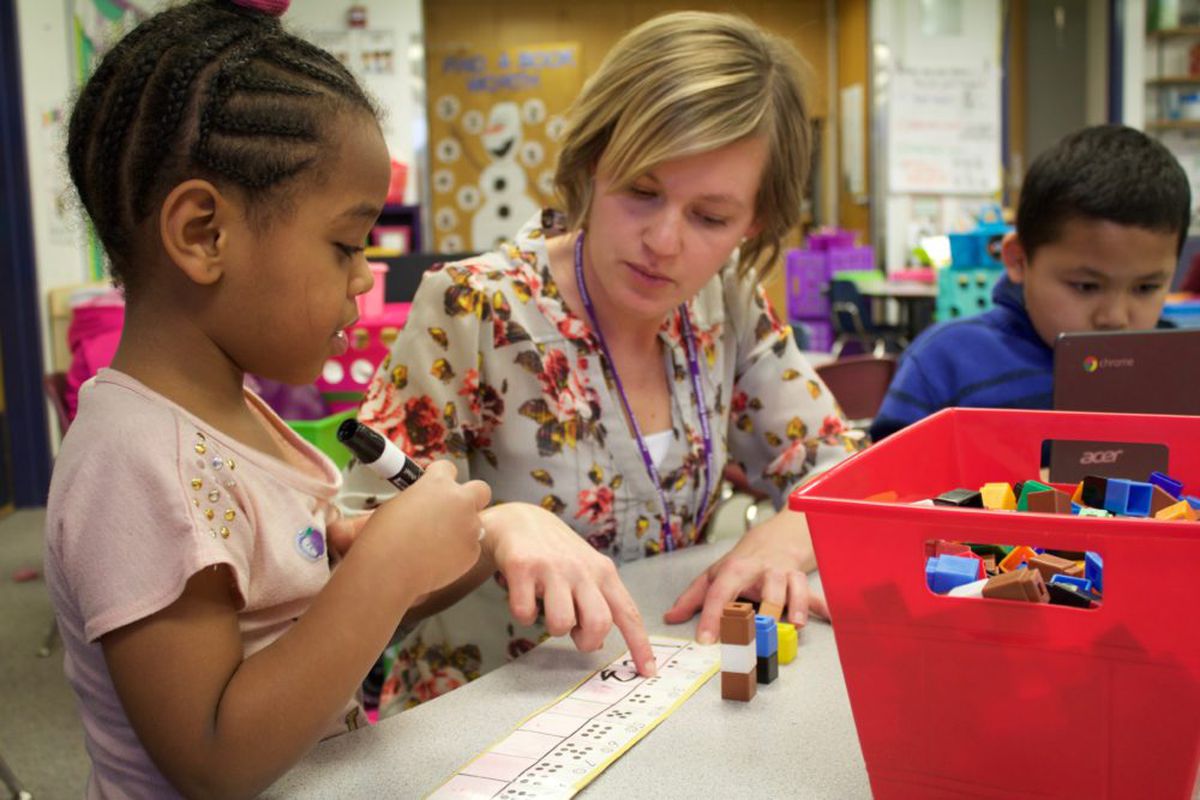 A kindergarten teacher at Kenton Elementary in Aurora, Colorado helps a student practice saying and writing numbers.