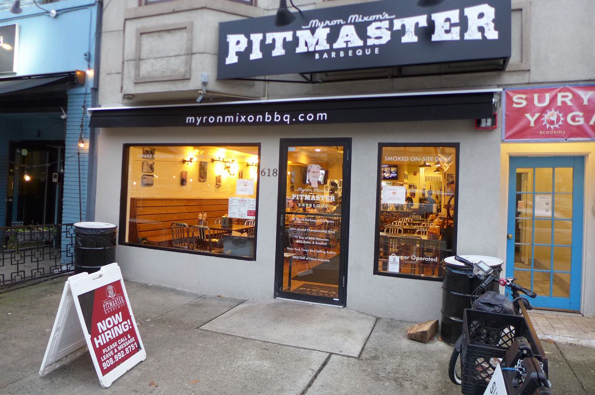 A storefront lit from the interior at twilight, with the word Pitmaster biggest on the sign at the top.