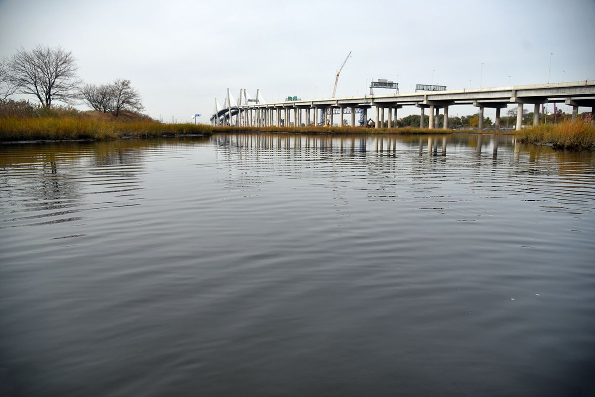A body of water with plants growing on either side. A bridge with traffic signs is visible in the distance. 