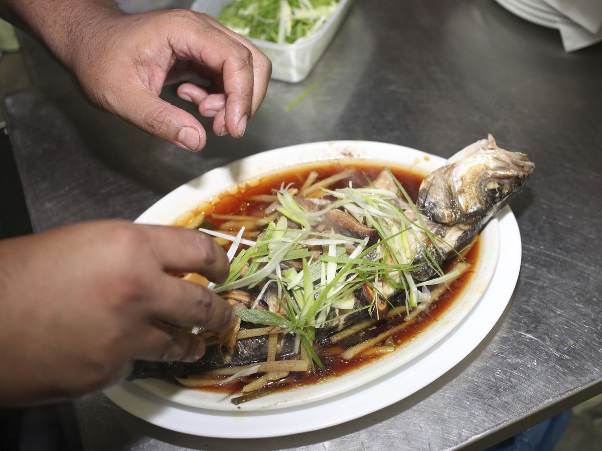 A chef adds fixings to a whole fish dish. 