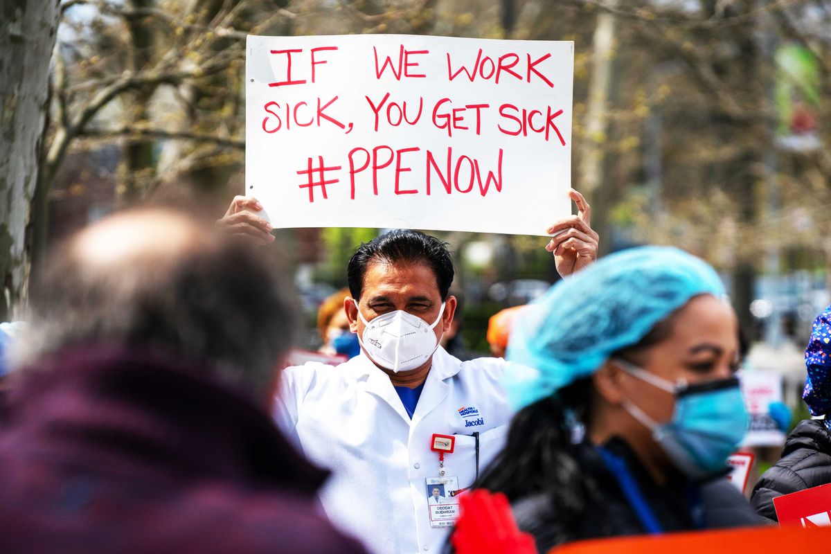 A protester wearing a breathing mask holds a sign that reads, “If we work sick, you get sick #PPEnow.”
