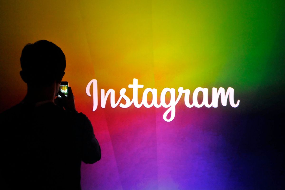 A silhouette of a person holding up a phone to take a picture of an Instagram sign backed by rainbow colors.