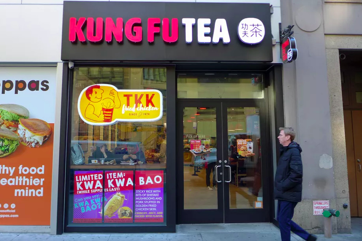 An exterior shot of a small New York City storefront, a combination TKK Fried Chicken and Kung Fu Tea location. A man in a winter coat walks by.
