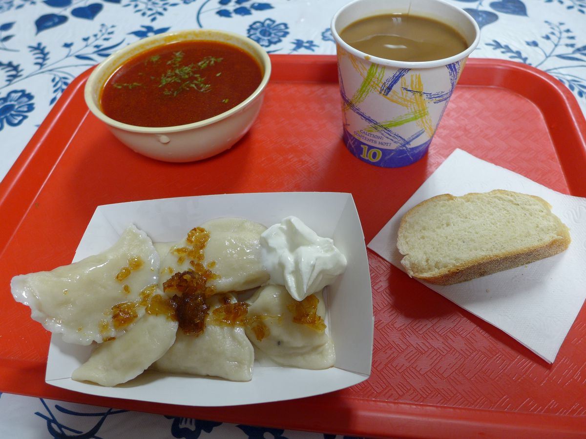 An orange tray with paper boat of pierogis and cup of purple borscht.