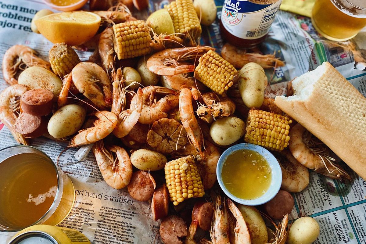 Corn, shrimp, potatoes, andouille on newspaper in a shrimp boil, with Crystal hot sauce and beers