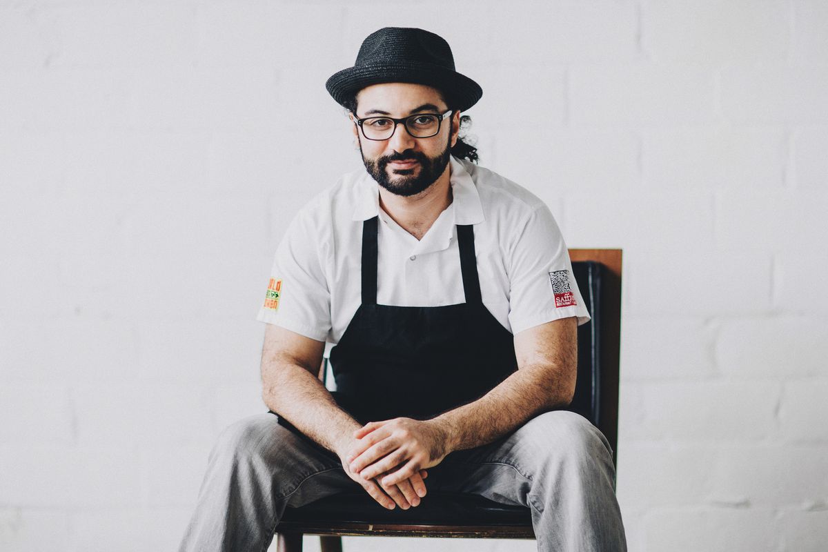 A picture of Wadi sitting on a chair in a white kitchen coat with a black apron over it