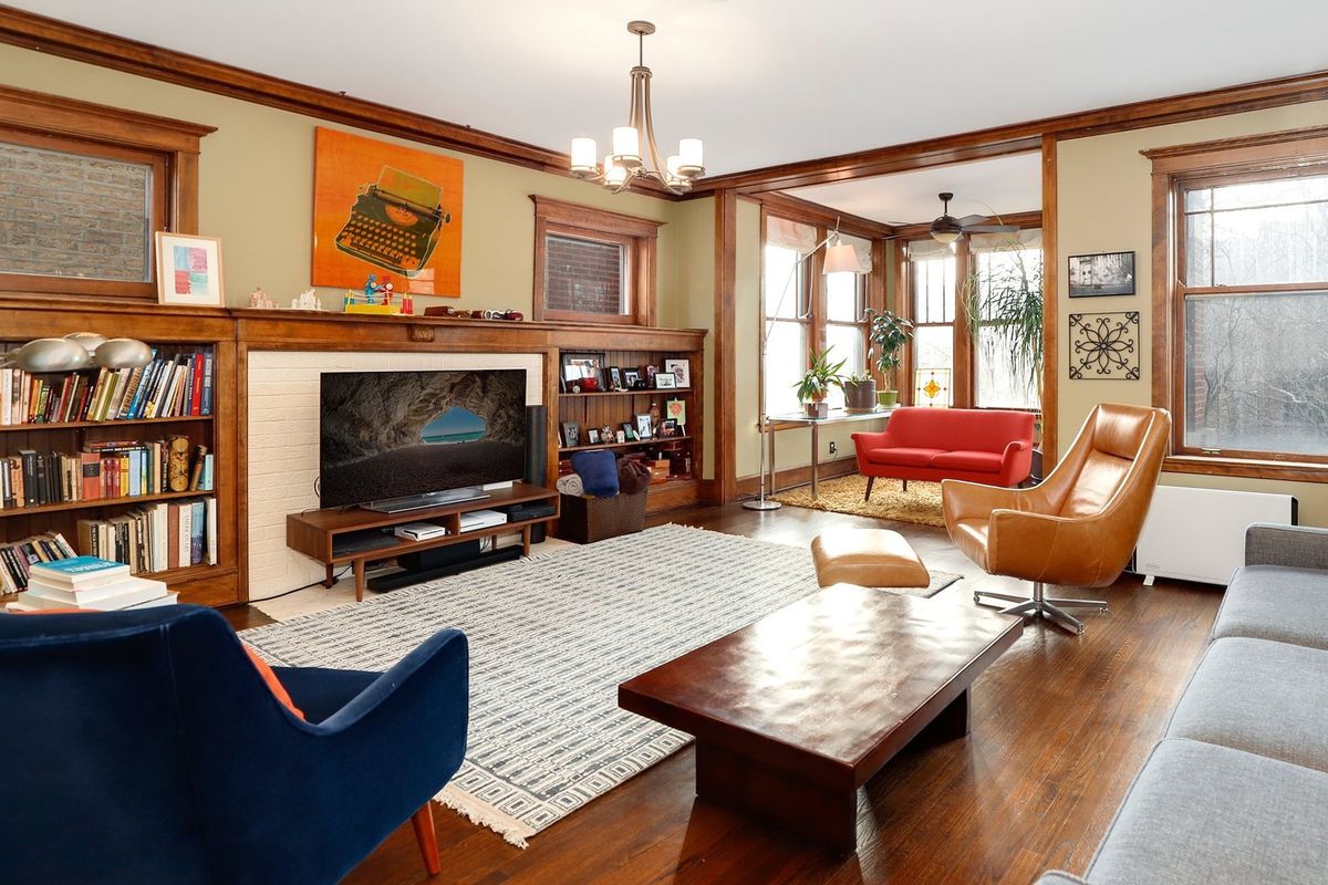 A living room with hardwood floors, a decorative brick fireplace flanked by built-in shelves, an area rug, coffee table, velvet chair, and sofa. 