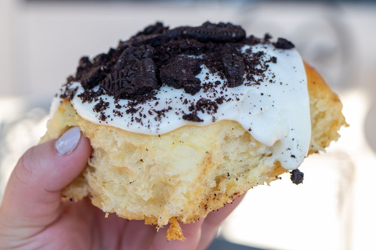 A baked good roll topped with white frosting and crumbled black cookies.