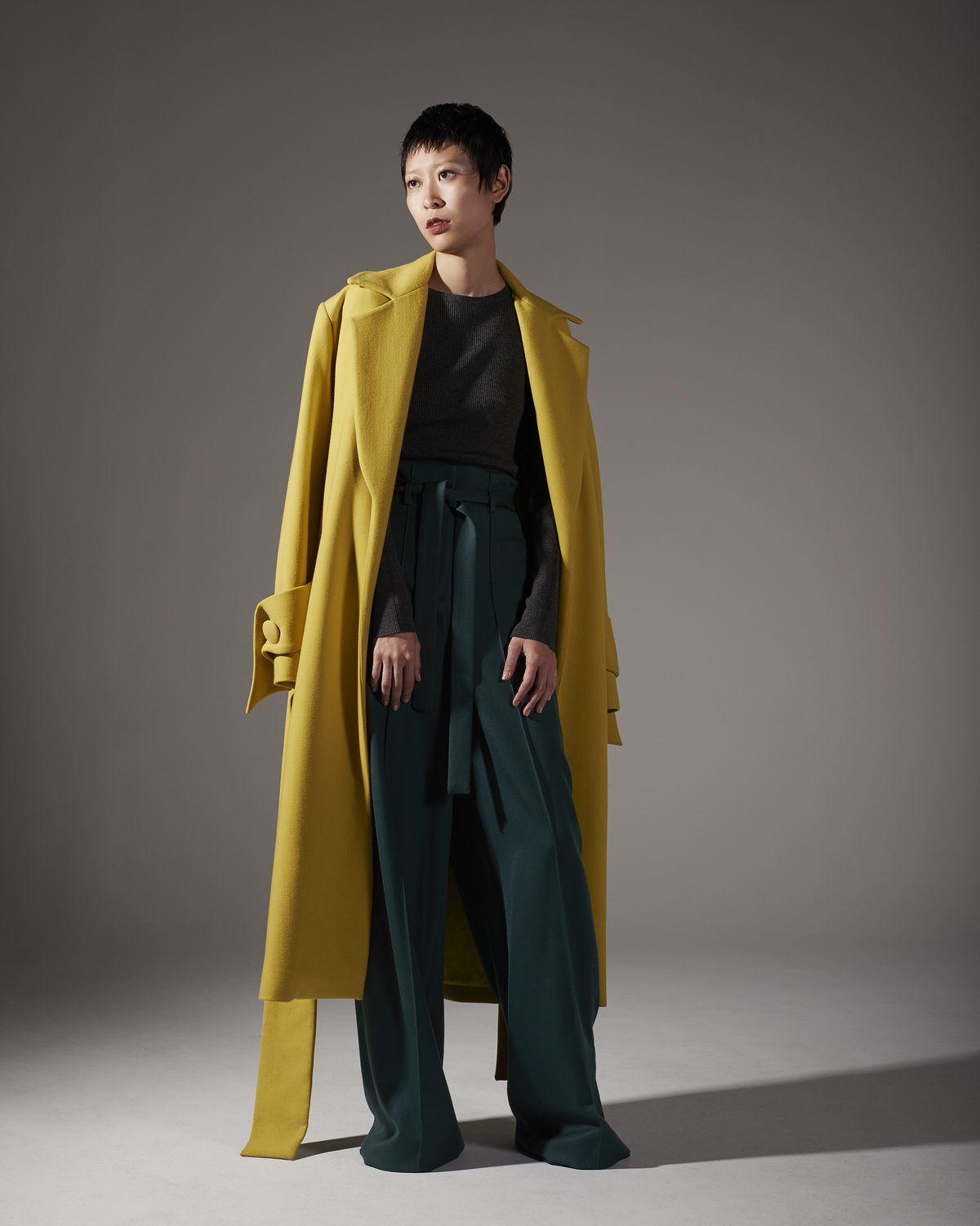 A model with short hair wearing a yellow overcoat and a green shirt