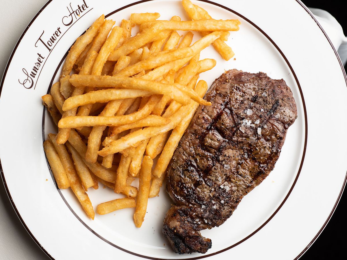 An overhead shot of a white plate with a cooked steak and pile of fries at Sunset Tower Bar in Los Angeles.