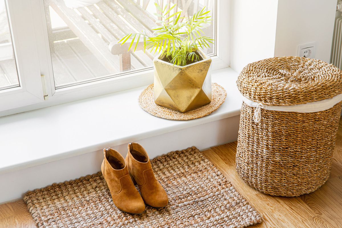 A decorative seagrass hamper next to a window with a plant and a pair of women’s shoes. 