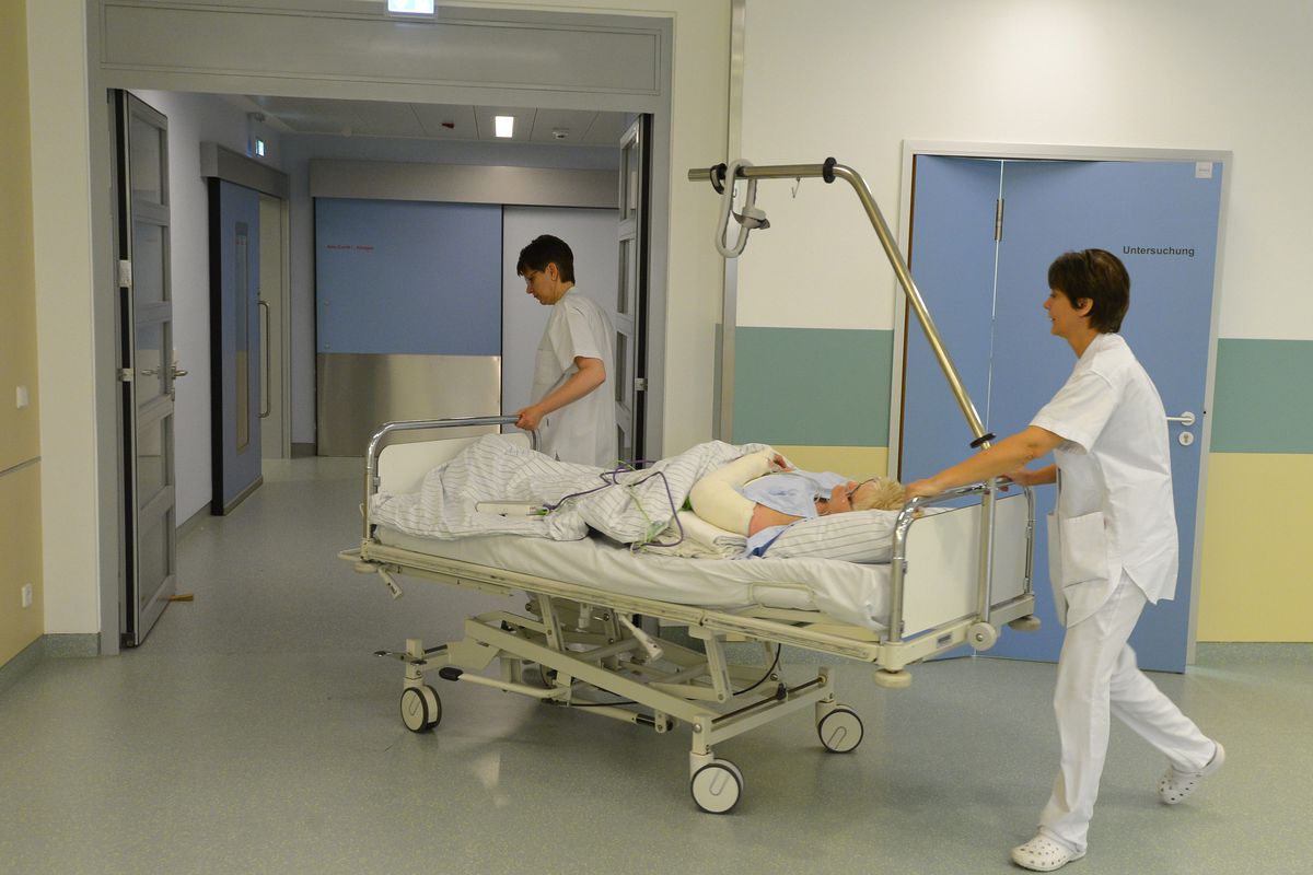 Two nurses roll a patient on a gurney down the hallway of a care facility