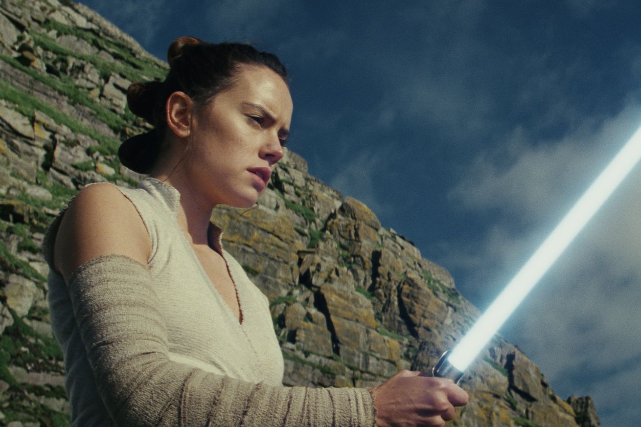 Daisy Ridley holding up a lightsaber in Star Wars: The Last Jedi.