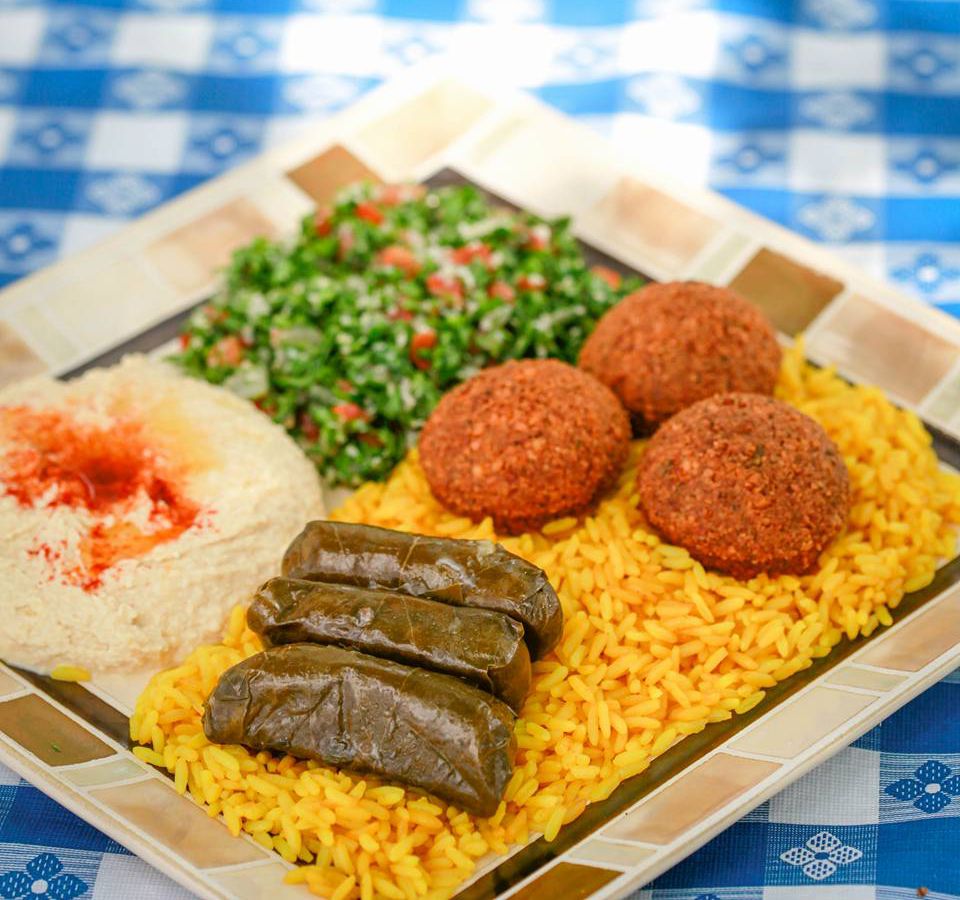 A plate of yellow rice, stuffed grape leaves, falafels, green salad, and hummus.