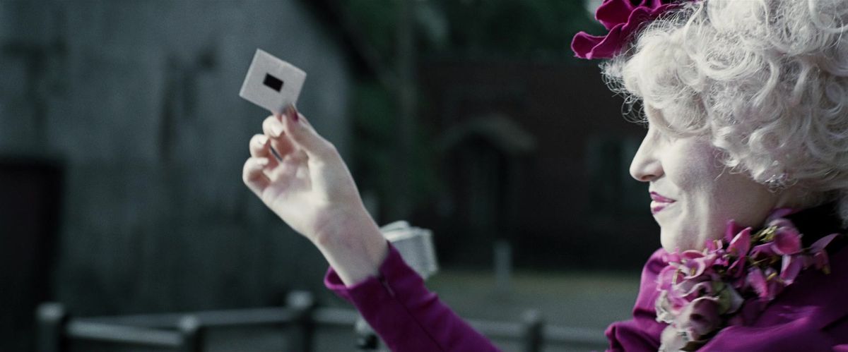 Effie Trinket holds up a slip of paper at the Reaping, taped shut in The Hunger Games film. 