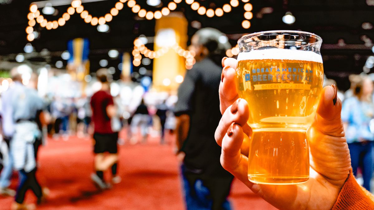 A close-up photo of a hand holding a souvenir tasting glass that has been filled with golden beer at the Great American Beer Festival.
