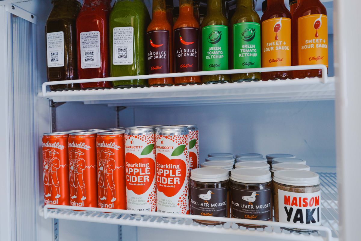 A refrigerator lined with hot sauces, duck liver mousse, and canned beverages.