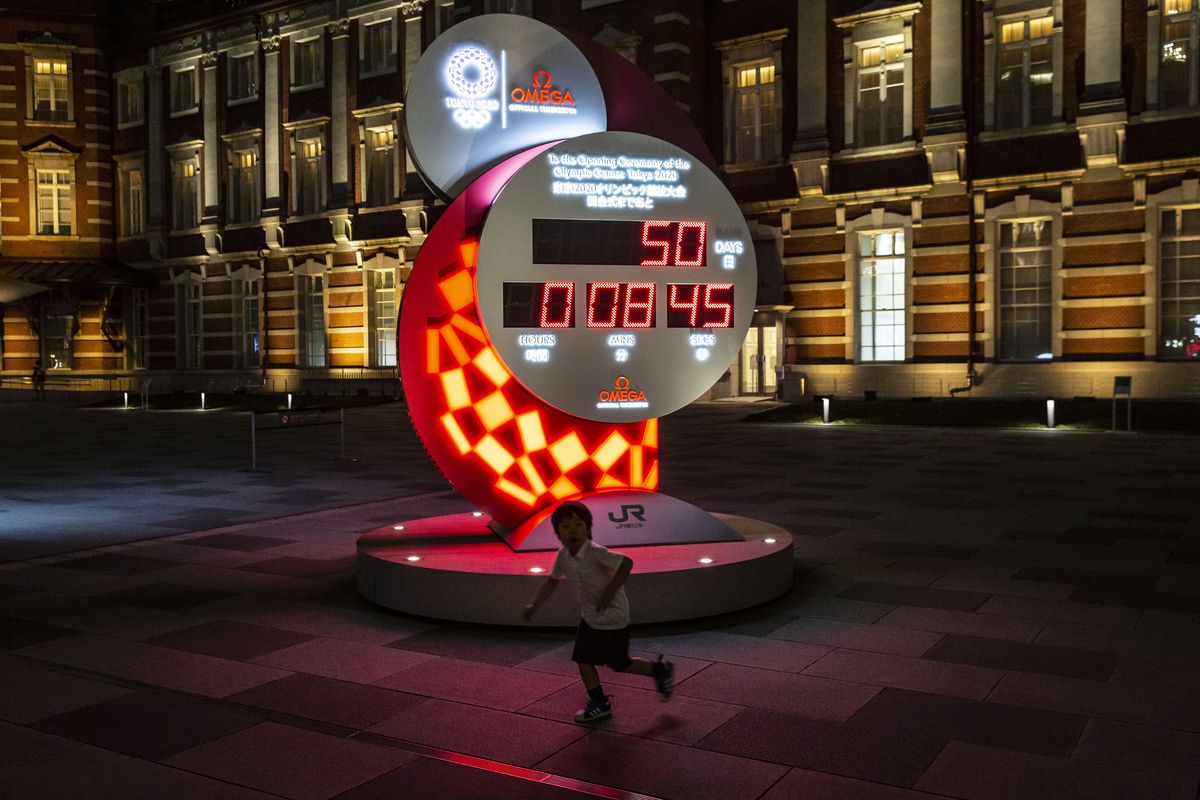 A child runs in front of a countdown clock for the Tokyo Olympic and Paralympic Games, seen at night on the day marking 50 days to go to the Olympic games on June 03, 2021 in Tokyo, Japan.