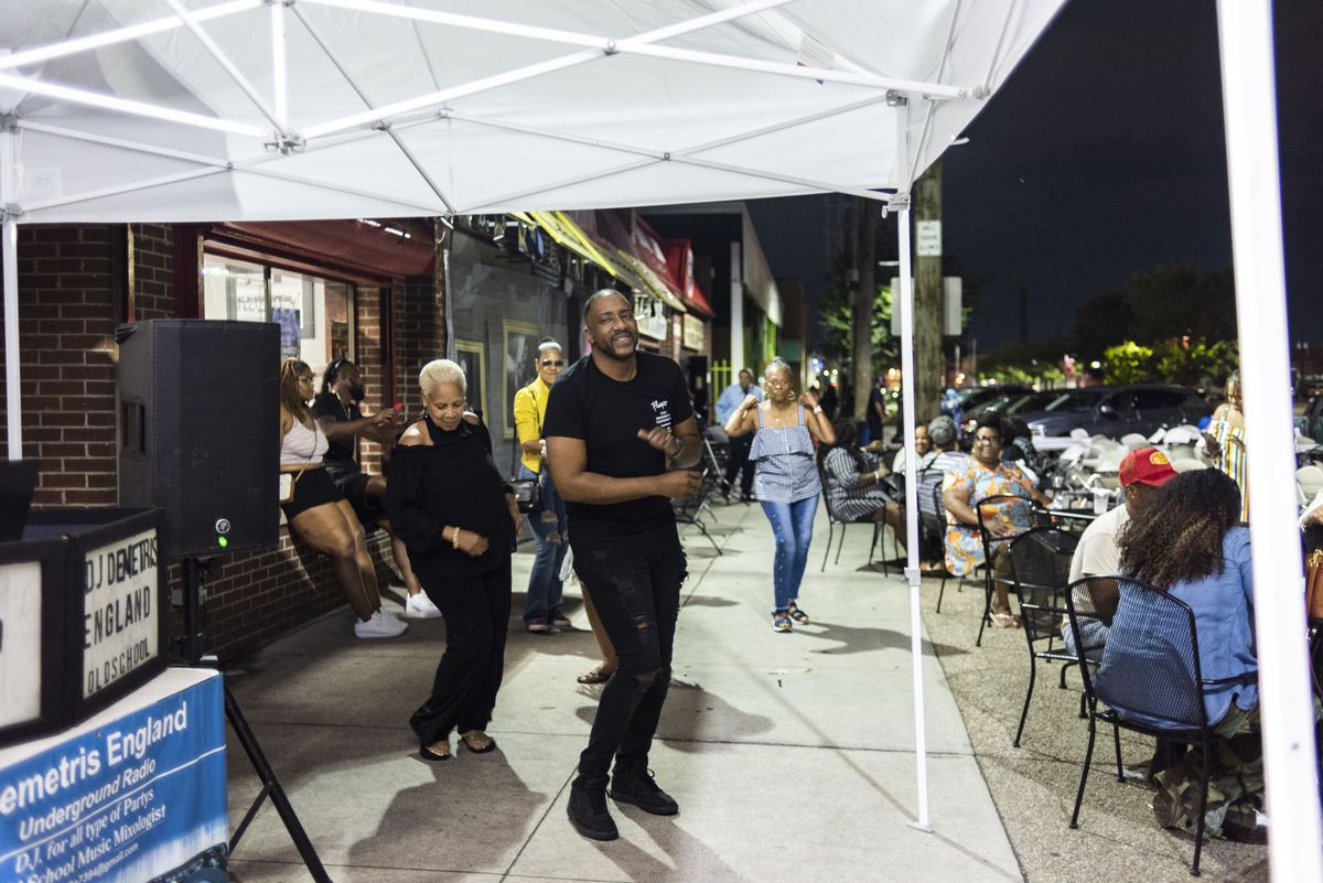 A man and woman, both wearing black, dancing outside of Bert’s Marketplace at Eastern Market in Detroit at night.