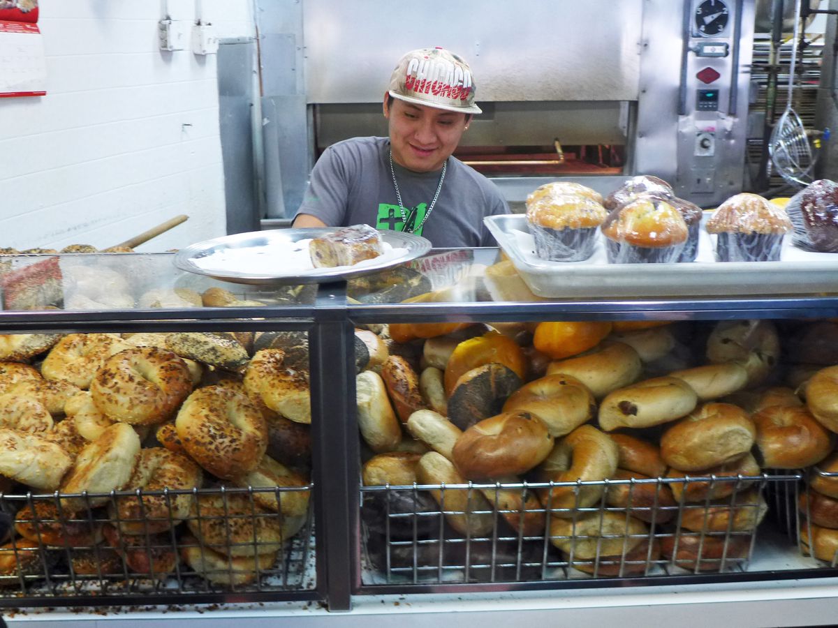 A man in a new year’s hat smiles behind a bagel counter.