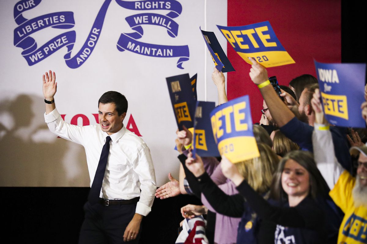 Former South Bend, Indiana, Mayor Pete Buttigieg raises a hand in greeting while supporters wave “Pete 2020” signs.