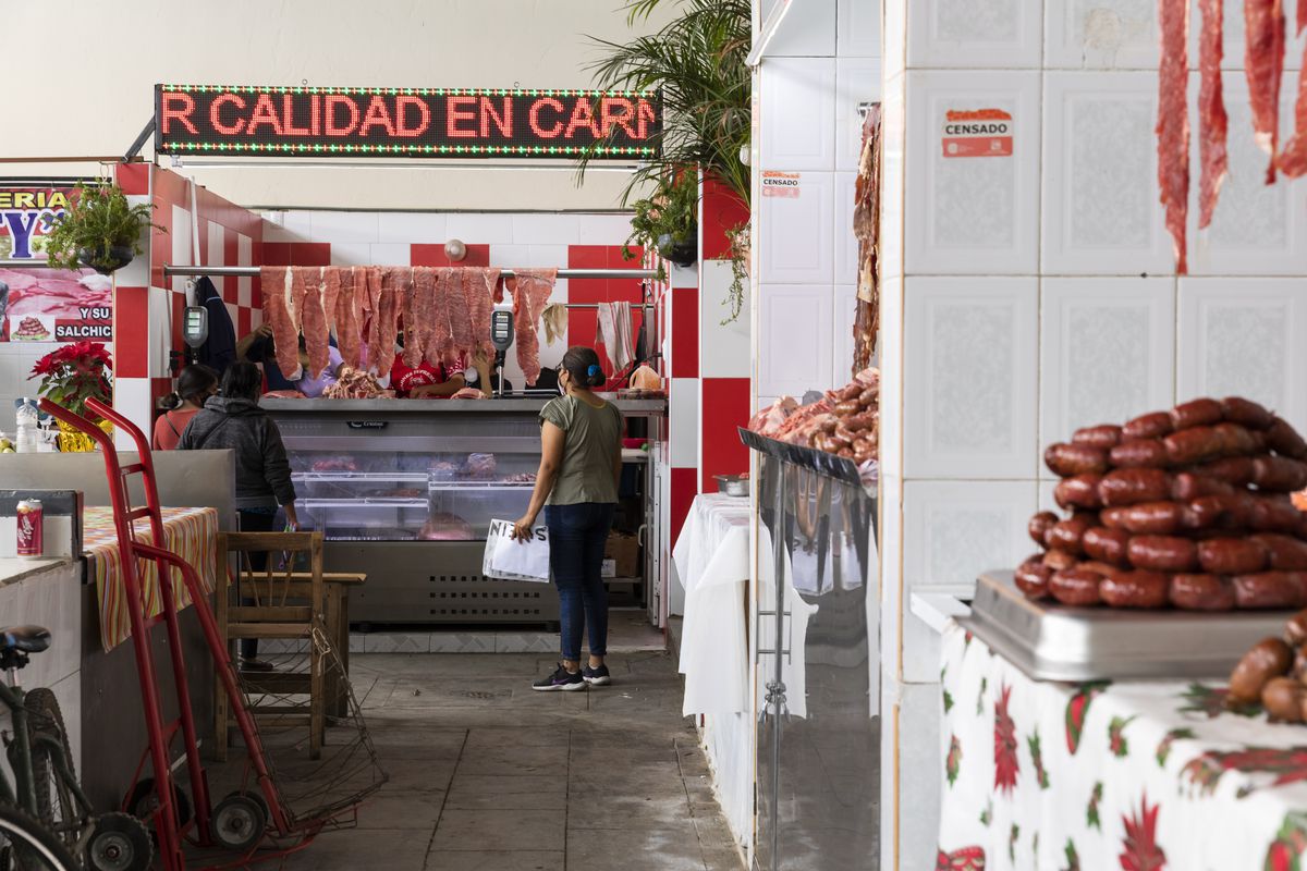 The interior of market, showing several stalls. One stall has a pile of sausages on display; another has slabs of meat.
