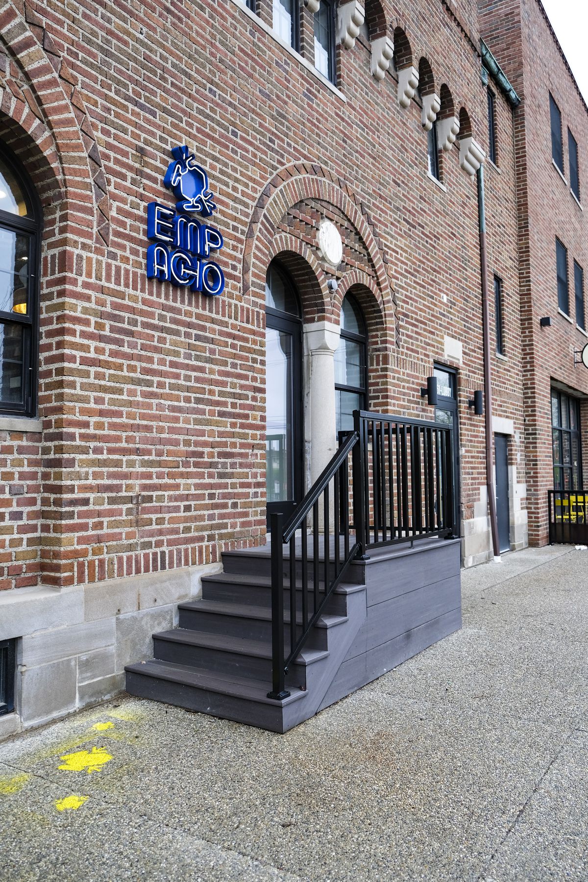 A brick building with a blue sign that says Empacho and features a blue frog, steps, railing, arched doorways at Empacho in Detroit, Michigan.