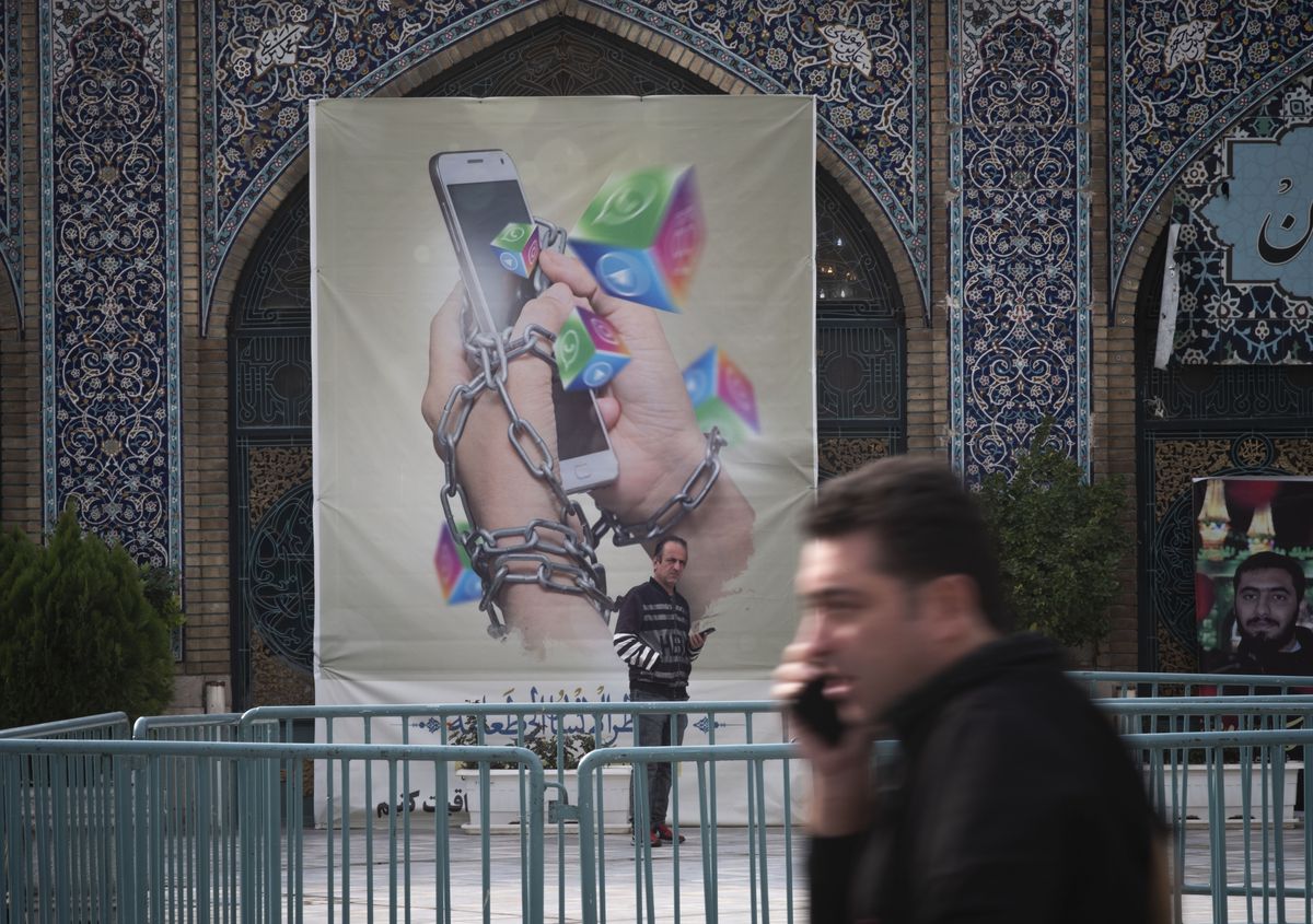 An Iranian man holding his smartphone looks on while standing under an anti-social networking banner in Tehran Grand Bazaar.