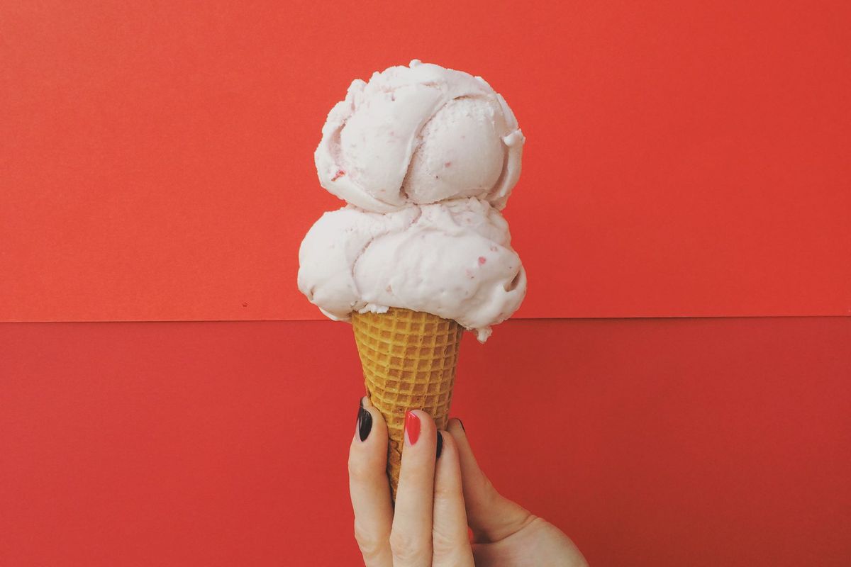 Two scoops of vanilla ice cream on a cone against a red background.