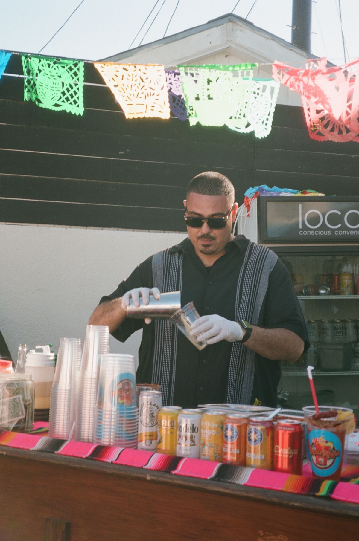 A bartender mixes drinks at a bar filled with cans and cups.