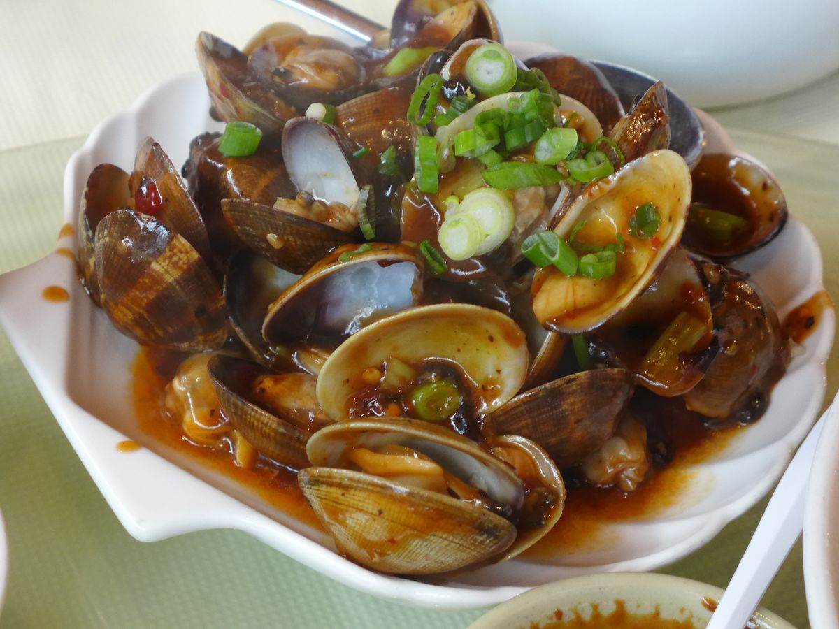 A jumble of clams in a bowl with chopped scallions and tiny black beans here and there.