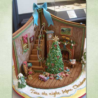 Gingerbread creation that displays the inside of a house with a Christmas tree next to gingerbread stairs.
