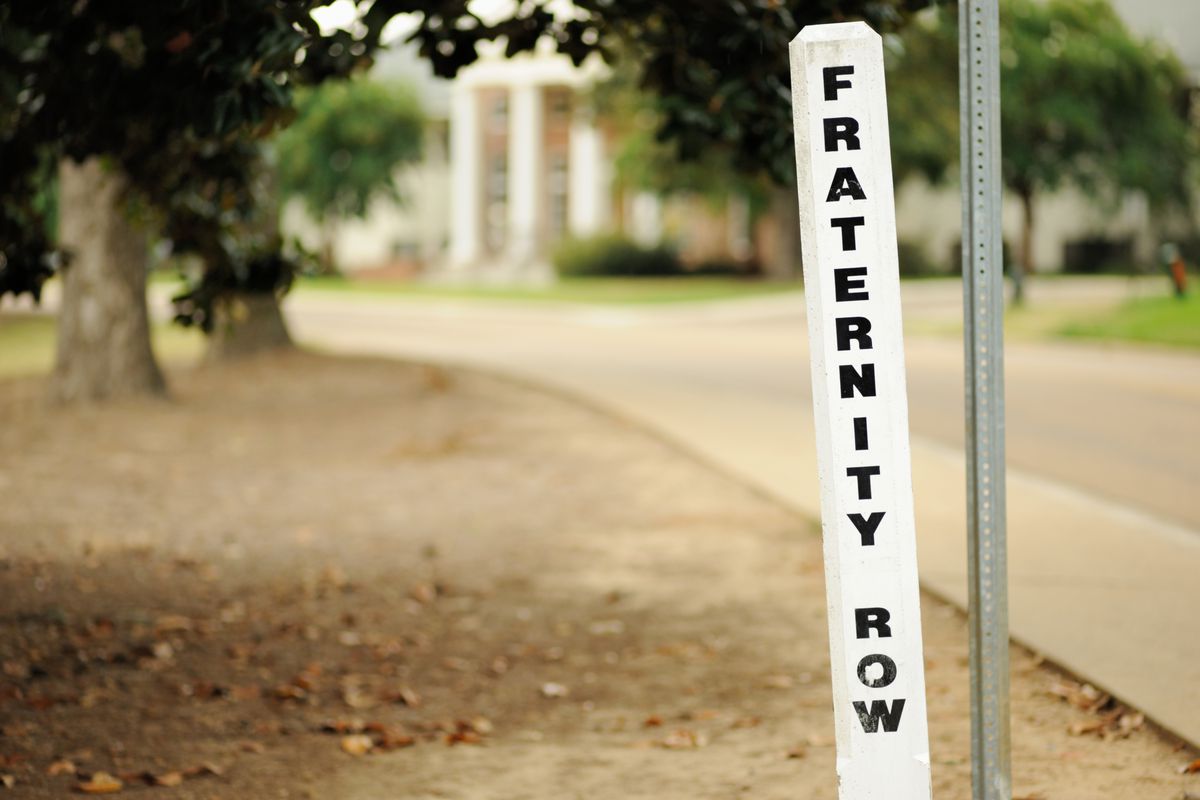 A signpost along a wooded campus drive reads “fraternity row.”