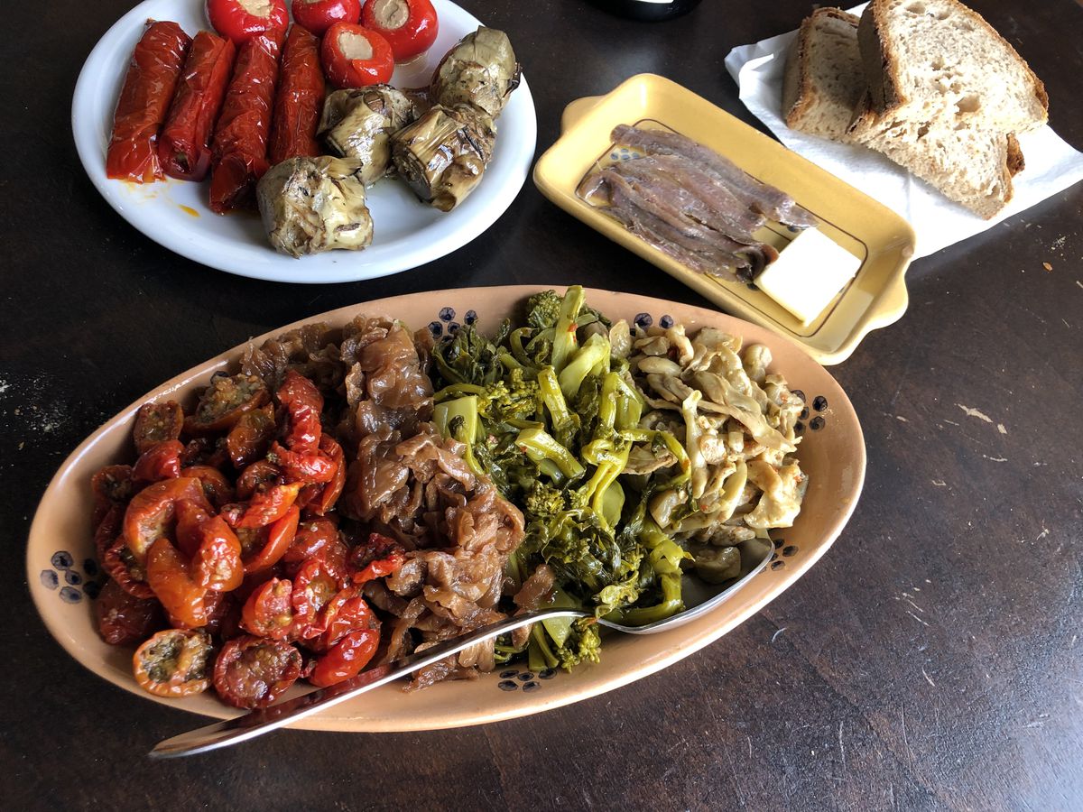 A large oval plate of vegetables, with small dishes of canapes, anchovies, and bread