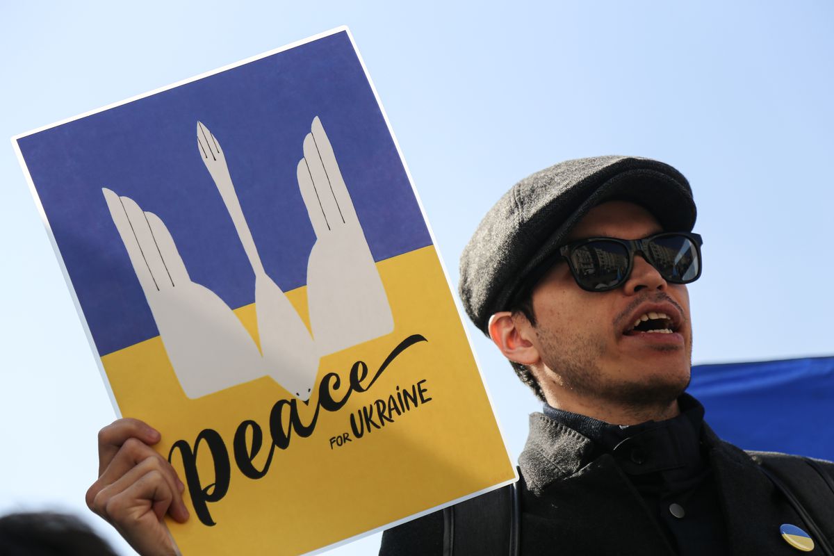 A man at a protest holds a sign in Ukrainian colors of blue and gold reading “peace”