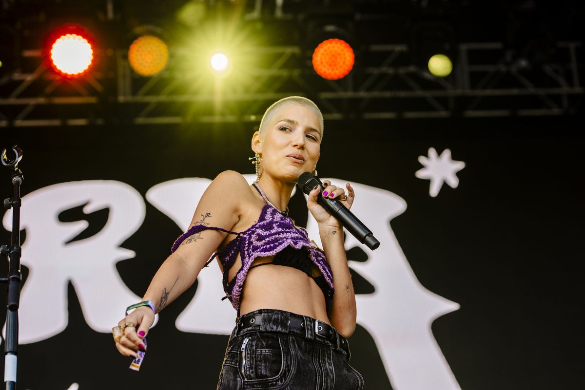 A woman in a pink-and-black crop top and black pants holding a microphone. 