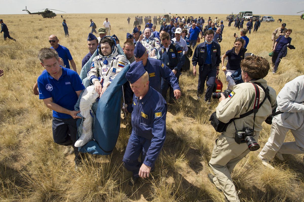 Russian and American astronauts are attended by medical and military personnel after landing in the Soyuz capsule.