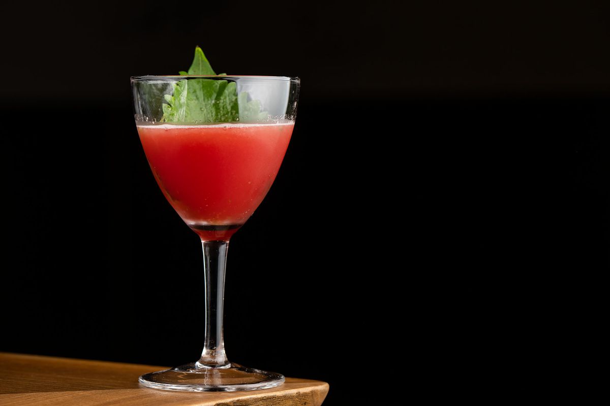 A red cocktail with a green leaf garnish.
