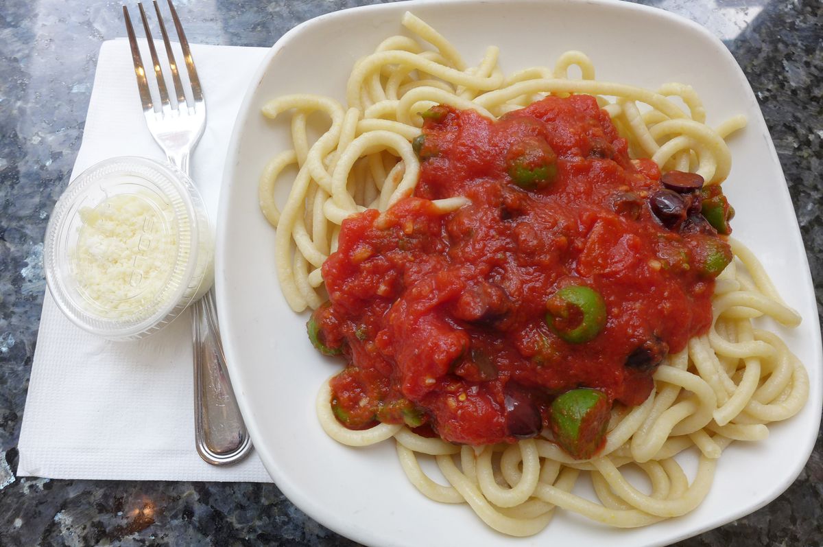 A plate of thick spaghetti with very red tomato sauce dumped on top and a small plastic container of cheese on the side.
