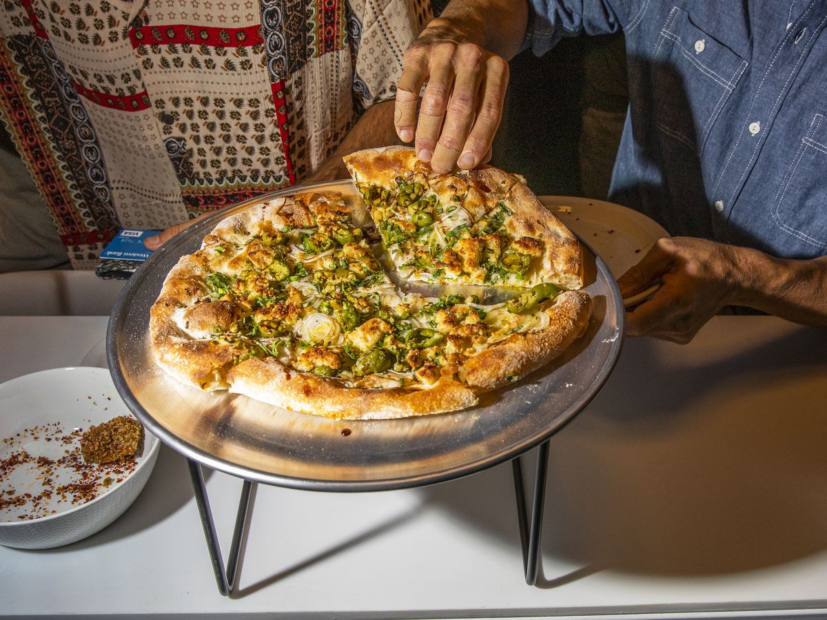 Person grabbing a slice of onion pizza with green olives.
