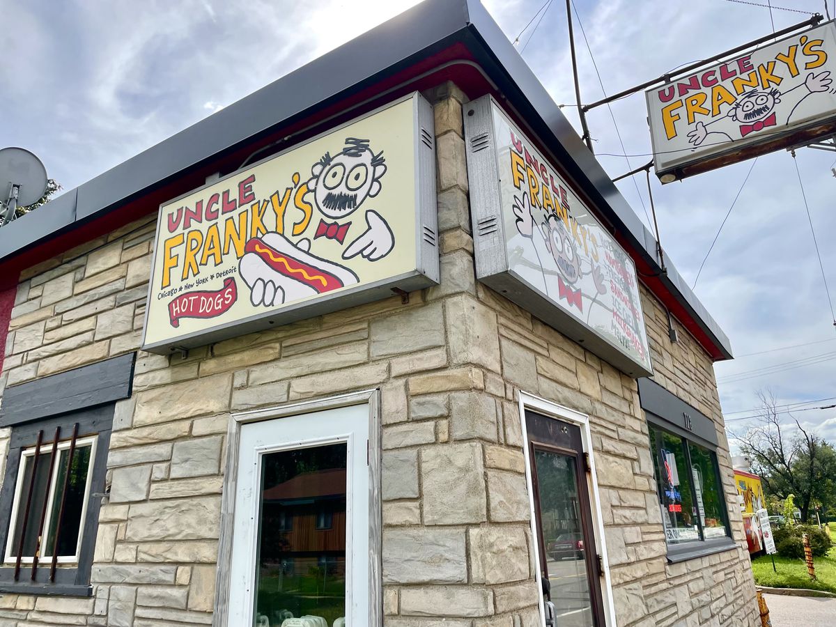 A brick building with signs that read “Uncle Franky’s” with a cartoon of a man with a mustache holding a hot dog. 