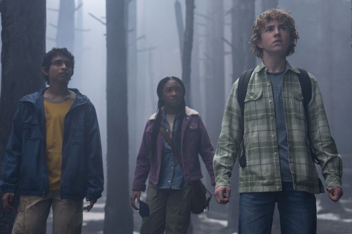 Percy (Walker Scobell) standing in the woods with Annabeth (Leah Sava Jeffries) and Grover (Aryan Simhardi), all looking up at something