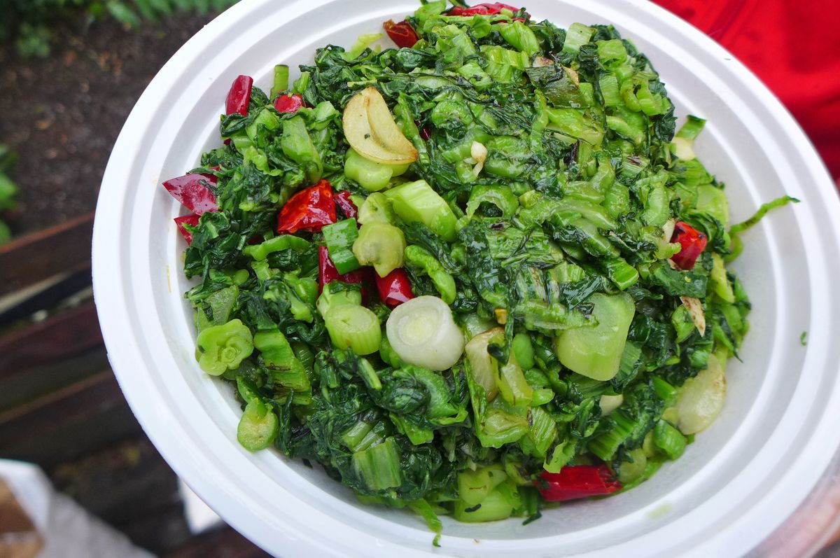 A white plastic bowl of greens dotted with red chiles.