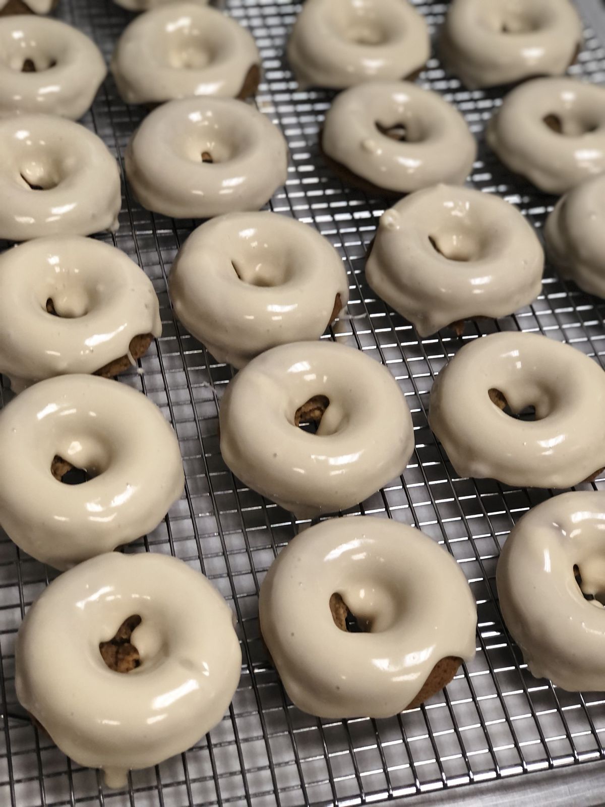 A long line of pumpkin vegan donuts on a baking sheet drizzled with white maple glaze.