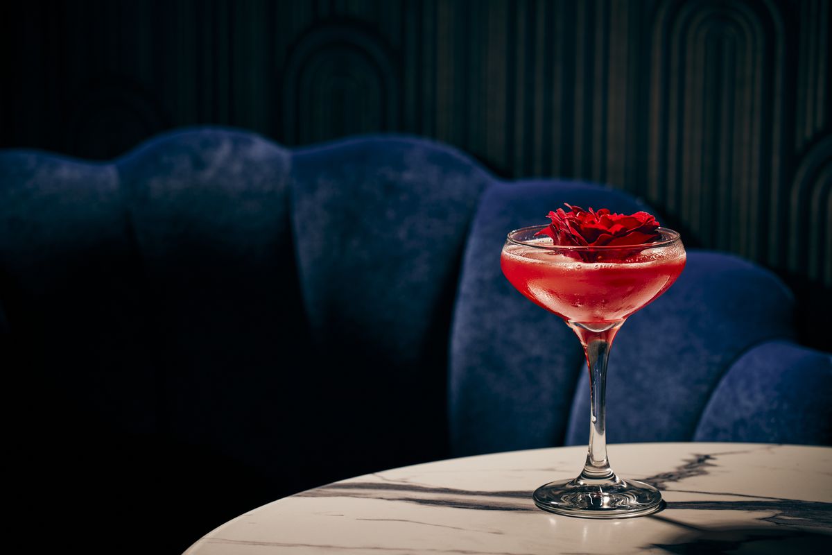 A red cocktail garnished with a red flower on a marble table.