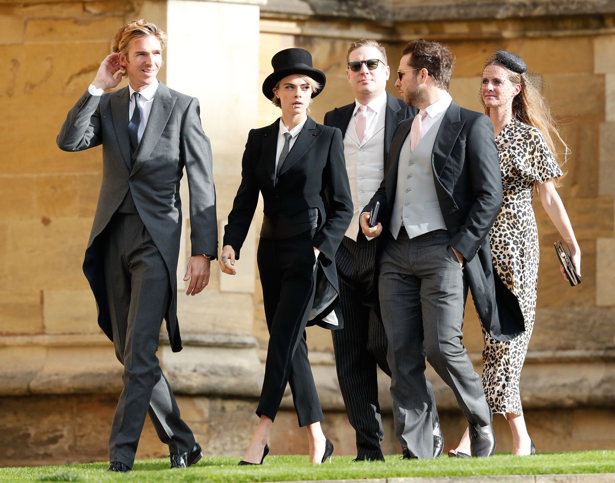 Delevingne wears a top hat, a tuxedo, and high heels.