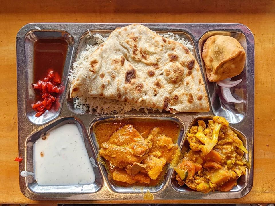 A silver tray of curries, naan, rice, and more sits on a wooden counter.