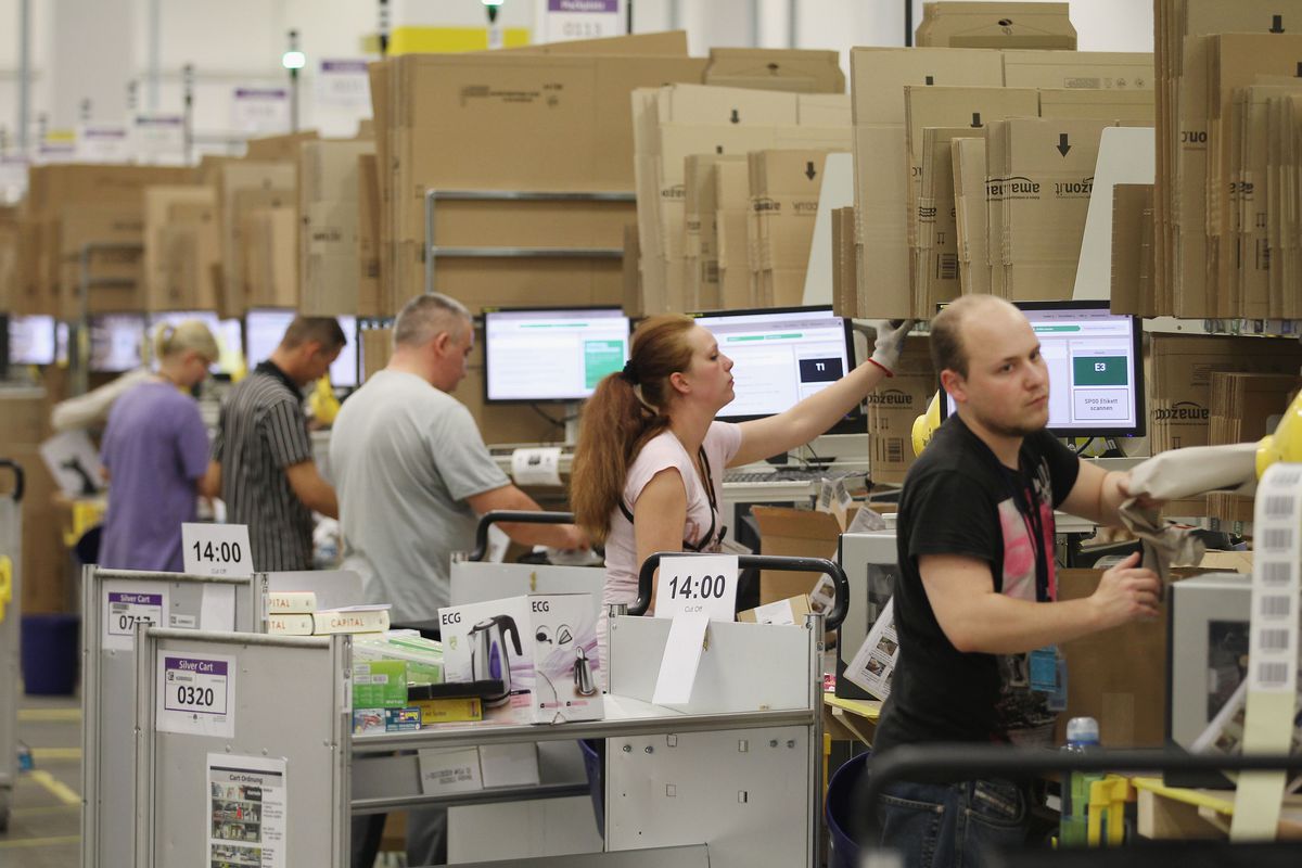 Several Amazon workers at a warehouse scan stacks of packages on the shop floor