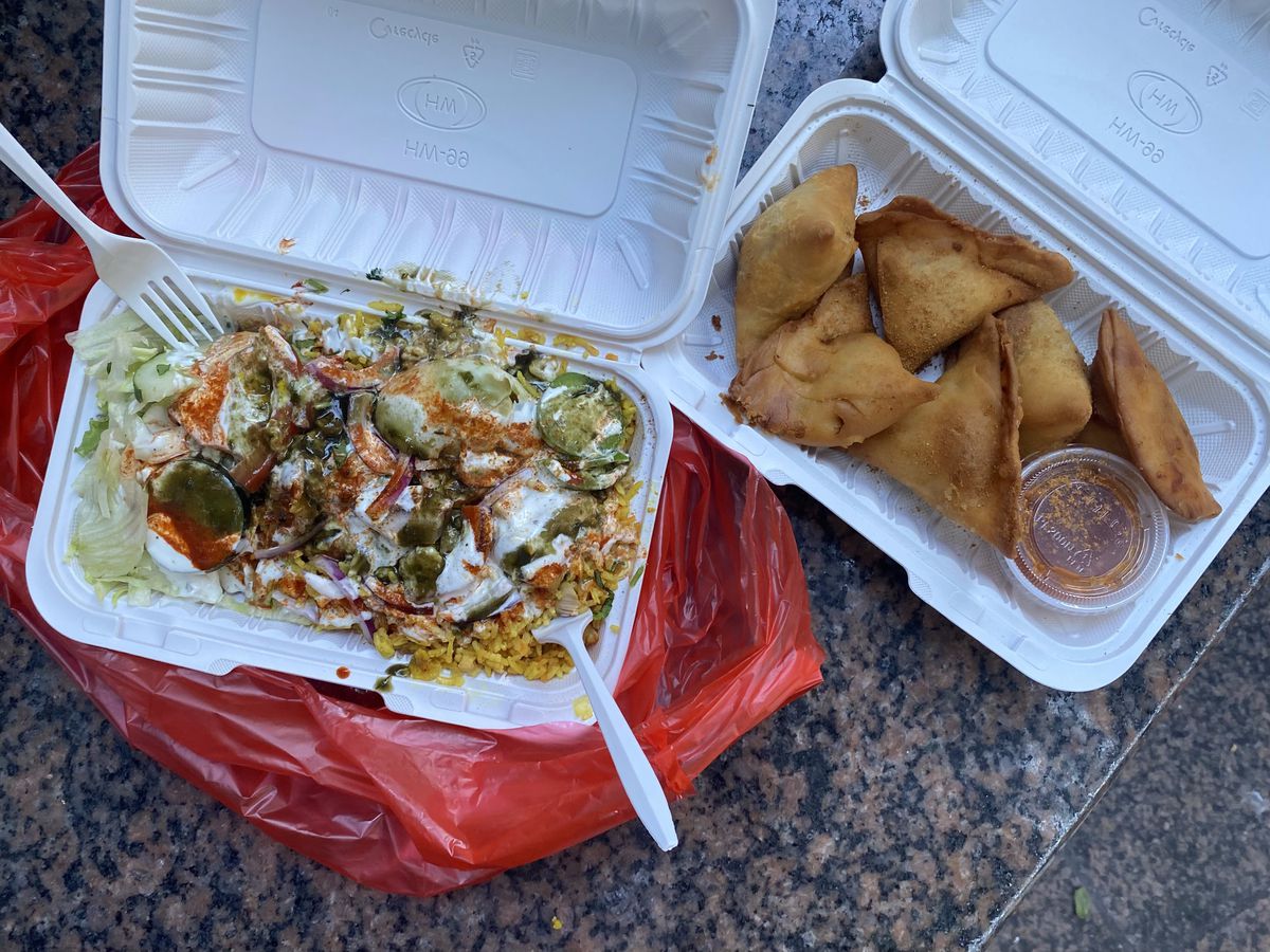 An overhead photograph of takeout containers with biryani and samosas.