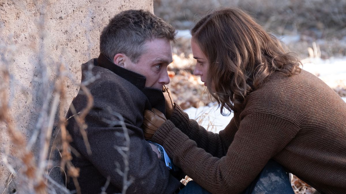J. Robert Oppenheimer (Cillian Murphy) slumps against a boulder outdoors, looking shaken, while his wife Kitty (Emily Blunt) grabs him by the lapels of his jacket and leans close to tell him to get himself together in Christopher Nolan’s Oppenheimer